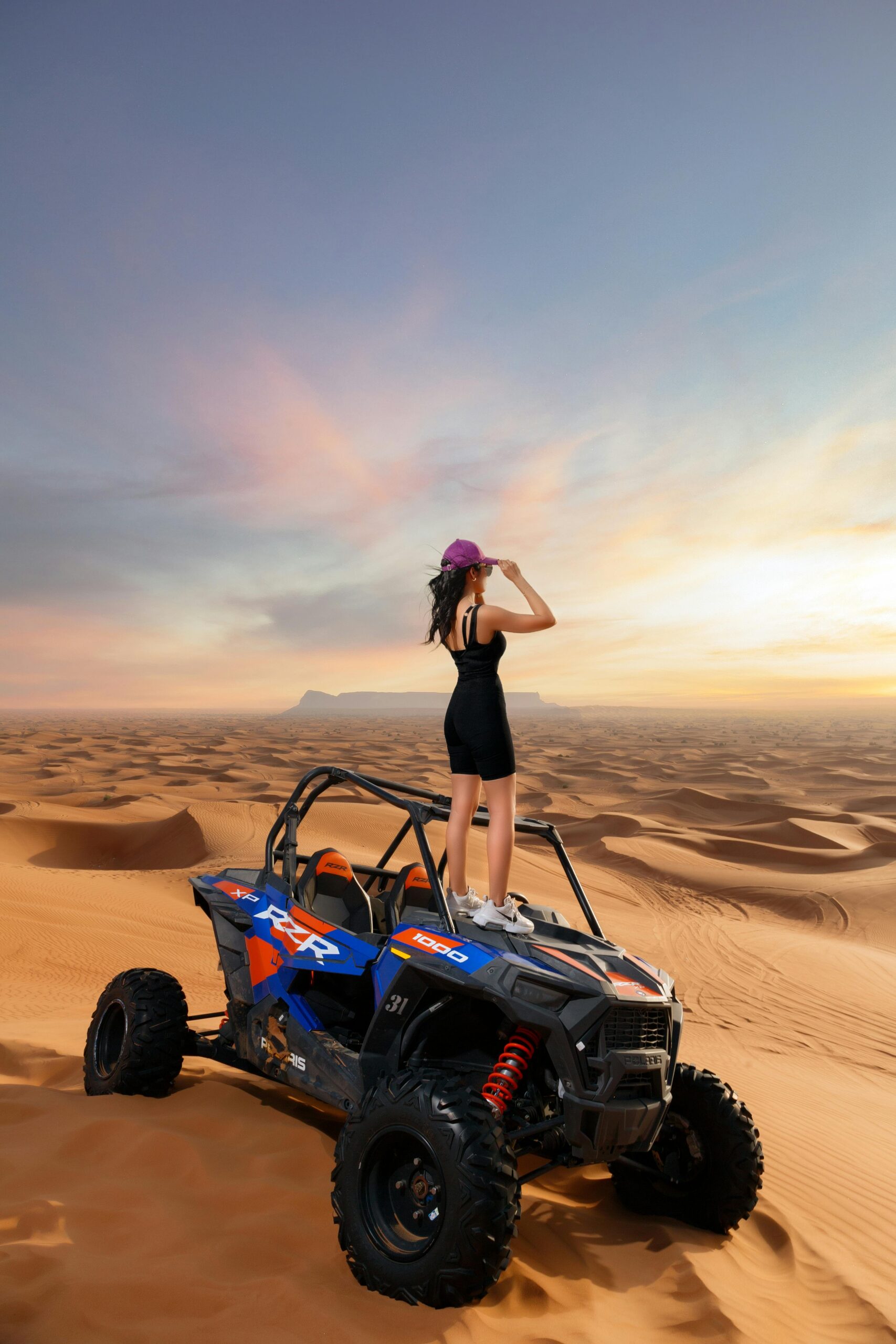 A woman stands confidently on an ATV amidst the vast sand dunes of Abu Dhabi, embracing adventure.